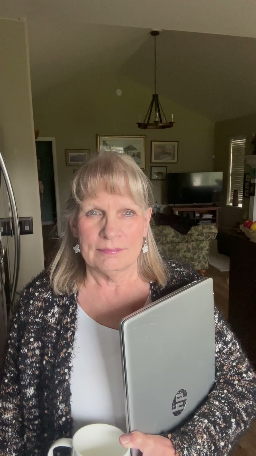 Carla holding her laptop and a cup of coffee at home, looking at the camera