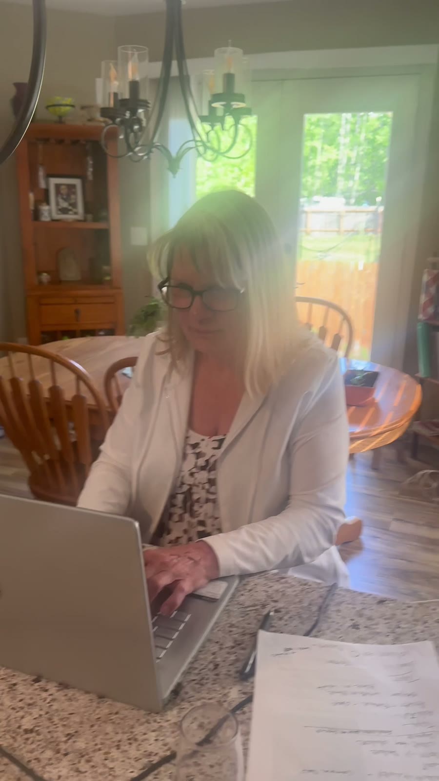 Carla in a white jacket working on her laptop at the kitchen counter